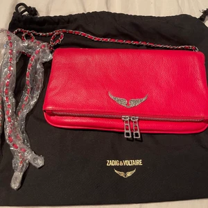 Zadig & Voltaire väska  - Säljer min nästintill oanvända Zadig väska. Färgen är röd och är helt slutsåld på hemsidan. Väskan är i den nya modellen av Zadig men även i den större modellen av väska . Har även 3 fack och ett mindre i. Dustbag och rem tillkommer.❤️ köpt för 3300 kr. 