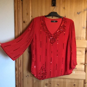 Härligt glittrande röd i stl 44 - Nyskick, alla paljetter kvar.  Frakt ingår