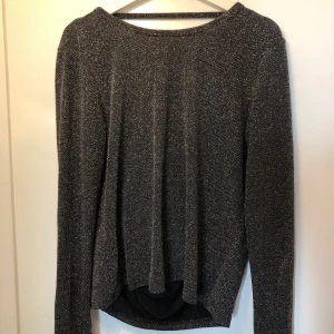 Glittertopp - Glittrig, långärmad topp. Man kan välja om man vill ha den djupa U-ringningen i bak eller i fram och ser fantastisk ut på bägge sätt. Mycket fint skick!