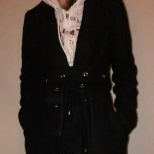 Skitsnygg kappa - Skitsnygg hel svart kapp från nakd. Kappa har ett svart skärp i midjan med silvriga öljetterna, skärpet sitter inte fast i kappan så om man inte vill ha skärpet så är det bara en helt vanlig svart kappa. Kappan går ner till vaderna på mig och är 168cm. Köparen står för frakt💕