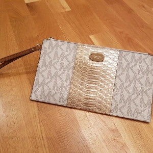 Michael kors  - Underbar liten praktisk väska som är perfekt till såväl fest som vardag. Gulddetaljer och ormtextur i mitten fram. En hel del fack som gör att alla vip-kort får plats ;) 25x14cm. Bara vristband. Oanvänd.