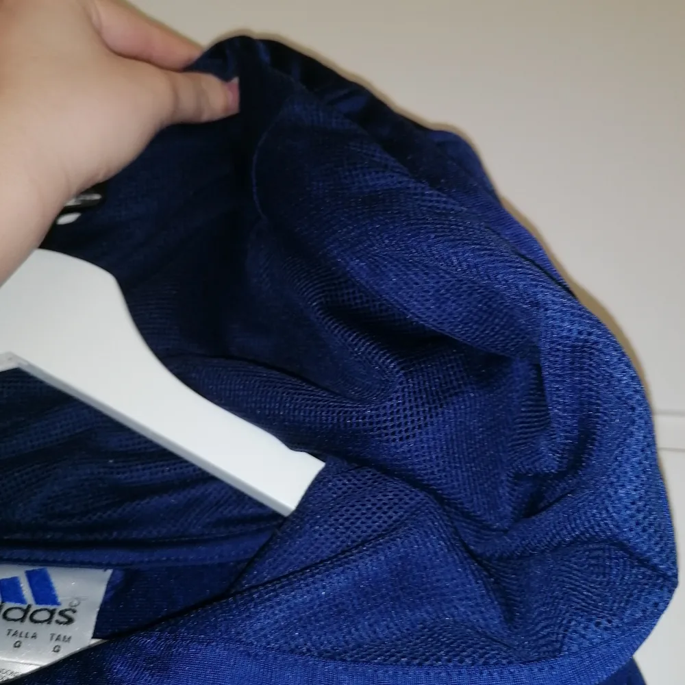 En marinblå Adidas tröja, tracksuit tröja med nät i huvan (se bild 3). Väldigt skön, storlek L därför används den inte av mig så mycket. Den är använd men väldigt fint skick enligt mig :) kommer ej ihåg om den är köpt på kill eller tjej avdelning. . Hoodies.