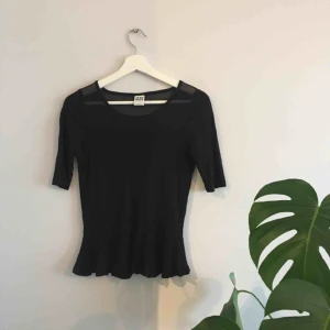  - Svart topp. En aning peplum-modell. Genomskinligt nät upptill och i urringning. 