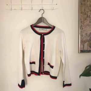  - Gräddvit finstickad kofta med röda och marinblåa detaljer och pärlknappar. Endast använd ett fåtal gånger. Kan mötas upp i stockholm. Annars står köparen för frakten:)