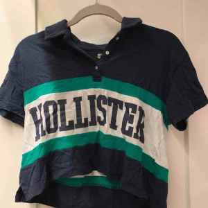 Tshirt - En croppad pikétröja från Hollister. Marinblå med gröna och vita detaljer. Snygg både knäppt och öppen. Köpt på Hollister i Nanjing när jag var i kina;) Stl XS men passar även en S. Så fin med högmidjade jeans! 50kr+ 30kr frakt.