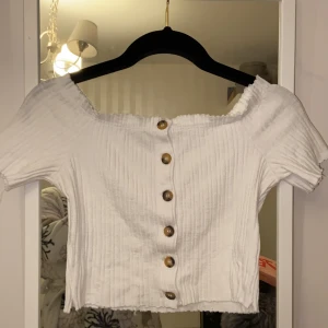 Top - En vit ribbad top med knappar som kan bäras som axellös. Använd ett par gånger men är i bra skick. Frakt ingår i priset