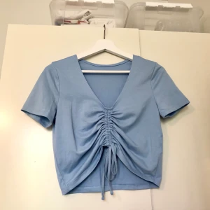 Ljusblå topp med dragsko - Baby blå topp med dragsko framtill, går att justera hur djup urringning man vill ha! Säljer pga aningen stor för mig. Färgen är som på första bilden, de andra bilderna är tagna på kvällen! Frakt tillkommer💞