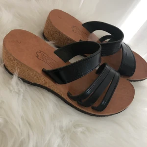 En riktigt fin handgjord äkta skinnsandal med korkklack sådär lagom hög. Stl 38 använda 2 gånger. - En skön handgjord ute eller innesandal i skinn  Använda endast 2 gånger då jag älskar skor och köper för många. Dom är handgjord utav en skinnmakare till mig när jag var i Grekland. Så dom är av riktigt fin kvalitet. Jag köpte två. De andra har jag kvar. Kanske inte säsong nu men det kommer fler eller använd dem inne.  Du står för frakt och swishar innan skick. 