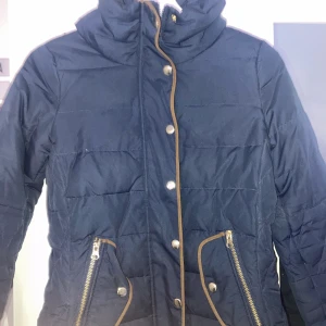 Jacka - Marinblå Höst/vinterjacka ifrån Vero Moda! Köptes för 4 år sedan! Ganska tjock därför passar den även väldigt bra till vintern. Fina bruna och gulddetaljer. Figursydd och går ner på midjan på mig som är 162 cm. Köptes för 1000 kr säljer för 450 kr! Köparen står för frakten