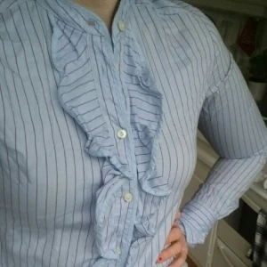  - Snygg blus i ljusblå /lila från Gant. Ostruken på bilden men volangerna är jättefina när den är tillfixad. Jag har använt den till tajta blå byxor eller kjol. Bra skick! 100 % bomull. Passar den som har 38-40 i strl. Nypris :1299kr 