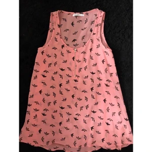  - En tunika/topp i siden material, något transparent. Bara använd en gång vid skolavslutning. Tunikan är en typ av starkt pigmenterad rosa, med svarta små fåglar som mönster. Framsidan är detaljerad med silvrig dragkedja. Den är i mycket bra skick! I med att den bara hängt oanvänd i en gradebråb hyfsat länge. Skriv vid intresse! 