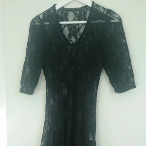  - Snygg klänning helt i transparent svart spets. Lång baktill, kortare framtill, sammetskant i urringningen. Fin att bära till fest över ett enkelt svart linne och kjol eller underklänning. Gott skick. Märke: style by tyra. storlek: M.
