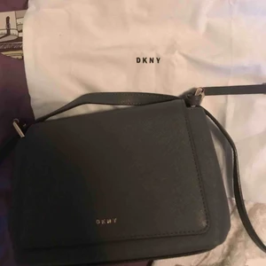  - Grå väska i bra skick från donna karan new york(DKNY). Går att ha både som axelremsväska och Cross body. Original-pris: 2000kr. Köpt på NK i Stockholm. Dustbag medföljer. Köparen står för frakt. Betalning via swish.