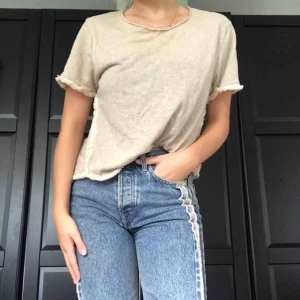  - En biege t-shirt med Frans-detaljer vid sömmarna🌾 super fräsch och snygg till allt!