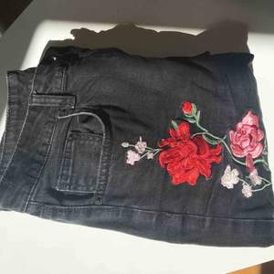 Svarta jeans med blommiga detaljer vid vänster smalben, höger höft och högra bakfickan. De är måttligt använda men fortfarande fräscha. 