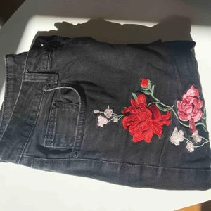  - Svarta jeans med blommiga detaljer vid vänster smalben, höger höft och högra bakfickan. De är måttligt använda men fortfarande fräscha. 