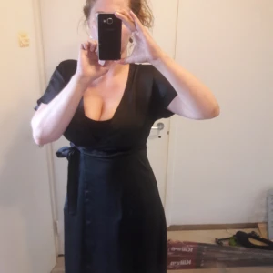  - Fin svart glansig omlott klänning från New Look. Helt ny och oanvänd med lappen kvar. Djur finns i henmet. Kan skickas mot att köparen betalar frakt.