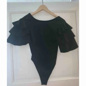  - Svart kortärmad body med volanger vid armarna! Aldrig använd!  Hämtas i Gävle eller fraktas, fraktkostnad tillkommer🌸