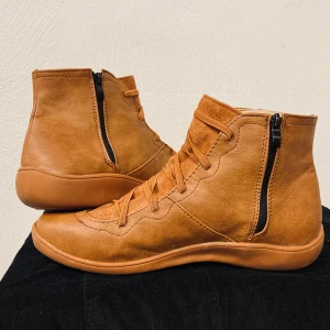 Fodrade, mjuka läderskor, nya, strl 41 - Ankelhöga skor av mjuk läder, lätt fodrade. Dragkedja på skornas insida samt snörning för att justera passform efter fotens bredd. Aldrig använda, normal strl 41. Finns i Sundbyberg men kan lämnas på annan plats i Stockholm alternativt skickas med post. Nypris 499 kr. Säljes för 179 kr