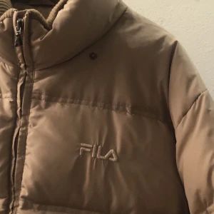 Fila vinter jacka - Super mysig dunjacka från Fila! Den har en skada, att det har funnits en liten detalj på grejen man drar upp dragkedjan med men den är bruten, inget är fel på själva dragkedjan så den funkar prima(se bild 3)! Köpt på humana. Kanske lite smutsig men de går bort i tvätten. Säljer pga kommer inte längre till användning.. + frakt, hittar inte vad det kostar men återkommer:) (tror det ligger någonstans runt 130kr)