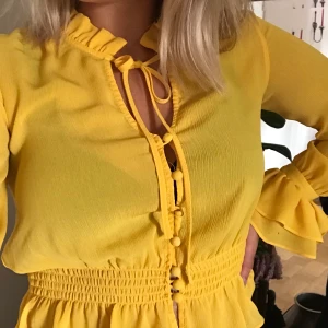 Gul blus - En jätte fin gul blus med knytning vid halsen och med volanger på ärmarna, runt halsen och vid midjan. Är sällan använd. Från Bikbok i storlek S.