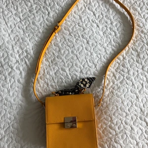 Gul väska med scarf från Zara - Gul jättesöt axelremsväska från Zara, med avtagbar scarf runt handtaget. I fint skick, bara använd ett par gånger. Kan hämtas i Malmö/Lundområdet alt postas för +39 kr frakt!