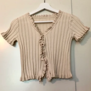 Ribbad cardigan med volangkanter - Beige cardigan med volangkanter och söta knappar. Väldigt fint men passar tyvärr inte så bra på mig! Köpt från YesStyle💞 Frakt tillkommer!