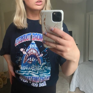 Tshirt - T-shirt med nån haj på, vet ej vart den är köpt då jag köpt second hand men tror den verkar vara köpt i Egypten. XL men går att styla snyggt om man är mindre än så :3 70kr + frakt (högsta bud ligger på 100kr) avslutar budgivning 15:30
