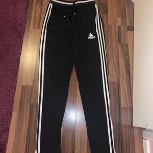 Svarta adidas byxor (trackpants) - Svarta sköna byxor från adidas som i princip är trackpants. Storleken är xs/s. Den är köpt på Stadium och är i väldigt bra skick då den ej kommit till nytta för mig. Den har dragkedje-slits på de 2 nedersta sidorna vid benen.