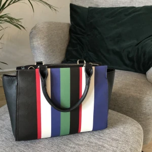 Randig väska  - Svart väska med ränder i olika färger på ena sidan. Mellanstor väska som är rymlig och i bra skick. Köpt i London för något år sedan men typ aldrig använt. 