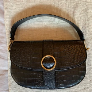 Svart handväska  - Skitcool svart handväska i ormmönster. Guldiga detaljer. Perfekt vardagsväska som rymmer allt det nödvändigaste och lite till. Väskan är i otroligt bra skick och ser helt oanvänd ut!! Köparen står för frakten <3
