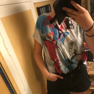 Färggrann top strl M/L - Färggrann top med fjärilar och strass 💕 O.P.L storlek M/L. Strechigt tyg och ganska lång, kan kanske användas som en tunika. Använd en gång🖤 (frakt ingår ej)