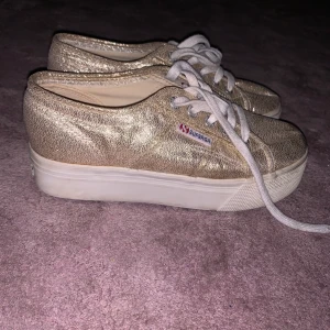 Superga skor med hög sula  - Superga skor i en guldskimrig färg med högre sula. Använd ett fåtal gånger så är i hyfsat nyskick. Bekväma att gå i trots att de är lite högre i sulan. Hör av er vid frågor:) 