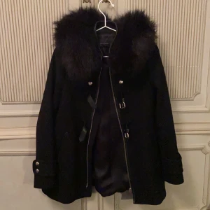Kappa med päls  - En kort svart kappa med (fusk) päls från Zara. Som man ser på tredje bilden är den avtagbar. Den har två coola spännen och dragkedja. Detaljer på ärmarna också. Använd men i gott skick. Nypris 899kr. Möts upp inne i Stockholm eller fraktar som du själv bekostar. 