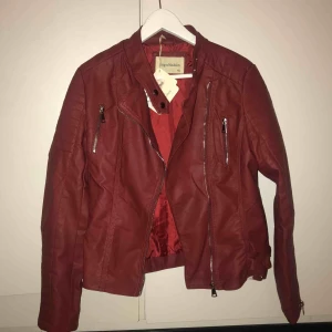  - Mörkröd skinnjacka, ordinarie pris 299kr. Har kvar skydd över ”bältespännarna”. Aldrig använd, prislapp sitter kvar. Storleken är XL men jag har s/m så passar folk med samma storlek. Säljes pga att jag inte riktigt tycker den är min stil.