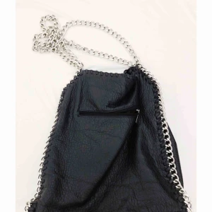  - Väska i skinnimitation med en metallänk som axelrem. En ficka på utsidan och en ficka med blixtlås på insidan samt ytterligare två fickor på insidan. Axelband 52 cm, bredd 32 cm, höjd 35 cm och djup 10 cm.  Aldrig använd, därför i nyskick. 550 kr nypris.