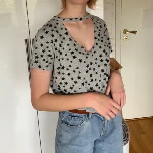 T-shirt med stjärnor  - Asball, grå t-shirt med svarta stjärnor och en utklippning vid bysten. Köpt i spanien så ganska unik. Storlek M men passar även S. Personen på bilden har i vanliga fall S. Kostar 50kr + frakt