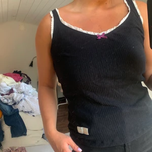 Oddmolly linne st 1 - Svart linne med vit söm och lila rosett på bröstet. I fint skick och i väldigt tunt och behagligt material! Frakt tillkommer