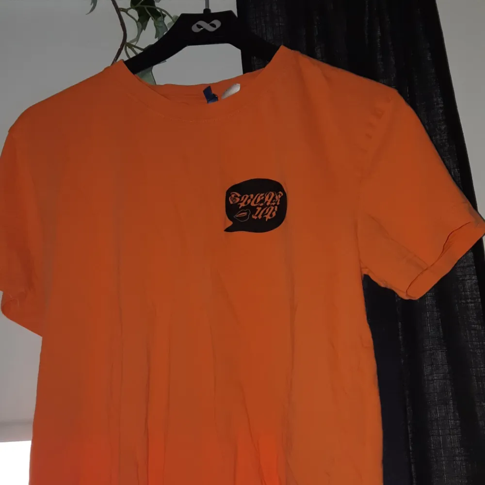 Orange t-shirt med svart tryck.  Det står 