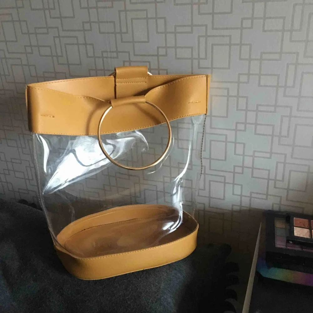 Cool genomskinlig vinylväska med senapsgula och guldiga detaljer❣️ Väskan inuti tillhör ett bälte och kan köpad till för 40kr. Köpt på boohoo för ett tag sedan nu men har inte blivit använd mer än 10 gånger, frakt tillkommer!. Väskor.