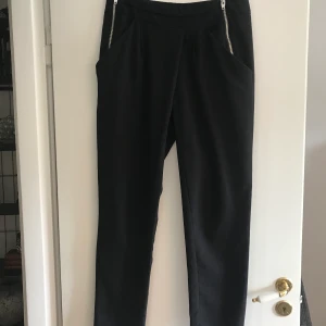 Snygga kostymbyxor med dragkedjor - Snygga kostymbyxor med dragkedjor på sidorna. Väldigt skönt löst material och hög midja.Fint använt skick. Färgen har försvunnit lite på själva flärparna på dragkedjan, ingen man märker om man inte tittar nära. Swishbetalning. Frakt ca 50:-
