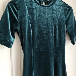 Klänning från Gina Tricot strl XS/S - Smaragdgrön klänning i plysch med hög hals och öppen rygg. Följer kroppen former väldigt tacksamt. Använd endast en gång. 