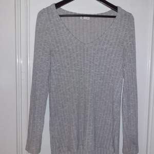 En grå,ribbad långärmad tröja i storlek M, tröjan har snittar på sidorna.