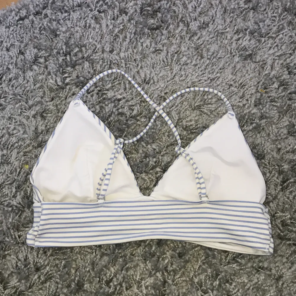 Bikiniöverdel från H&M med snörning i ryggen. Vit med blåa ränder, använd enstaka gång vilket resulterat i mycket bra skick. Kupan är 75B. Övrigt.