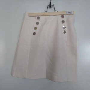  - Vit stilig kjol från H&M. Guldknappar framtill som dekor. Dragkedja därbak. Skick: Aldrig använd. Gratis frakt!