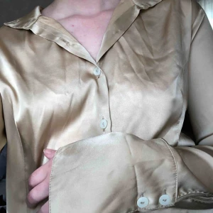  - Guldig skjorta med långa armar.   100% polyester  Vid köp kan vi antingen mötas upp i centrala Stockholm eller så betalar köparen frakten.
