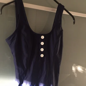  - Retro baddräkt, marinblå och vit med knappar. Har typ inbyggda shorts. Djup rygg.