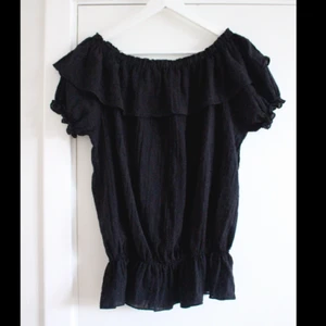  - Snygg svart blus med volanger och fina detaljer från Lise Sandahl. Helt oanvänd! Säljer även en likadan i vitt. 