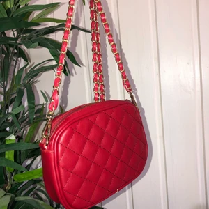 Axelremsväska  - Röd axelremsväska från Kappahl. Oanvänd därav nyskick. Har en mindre ficka med dragkedja på insidan. Axelremmen är ganska så lång. Säljer för 100 kr och köparen står för frakten (: