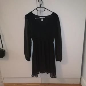  - Svart V-ringad kortklänning från NLY Trend. "Genomskinliga" ärmar i mesh-liknande tyg. Använd ett fåtal gånger.